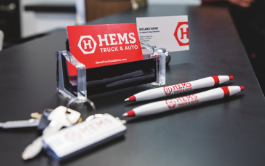 Marketing marterials such as business cards, pens, and keychains sittting on top of a black table.